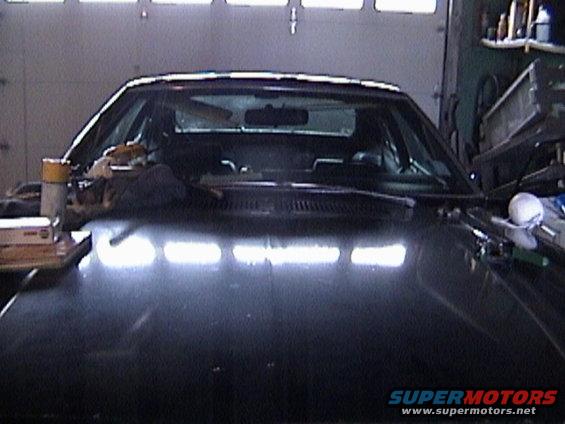 Black 1977 Ford Mustang II hood and windshield with items on dashboard