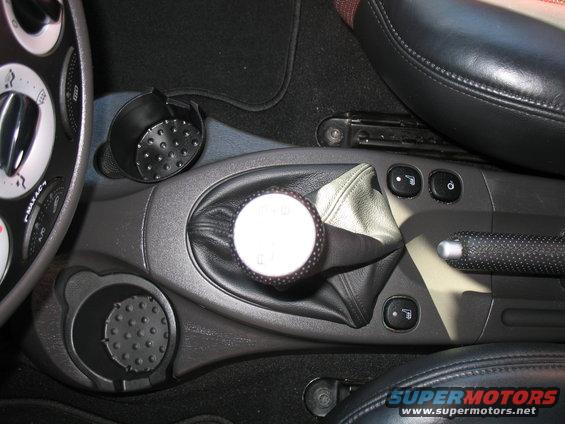 Car interior showing a manual gear shift knob, leather boot, cup holders, and climate controls