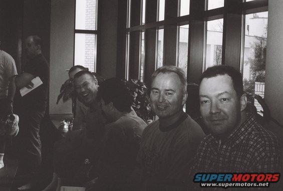 Group of men in a room with large windows, one man laughing, another smiling
