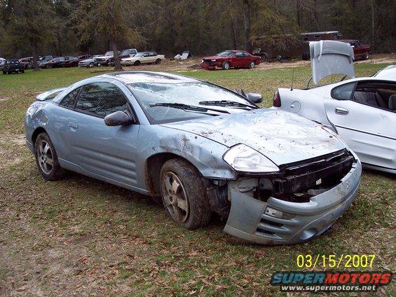 Light blue coupe with front end damage, parked on grass with other cars around