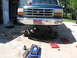 1974 Ford F-100 - Front suspension of a green Ford truck is being worked on, with parts laid out on the ground.
