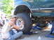 1974 Ford F-100 - Man works on a green Ford F-150 XL truck lifted on jacks, with another person assisting underneath.
