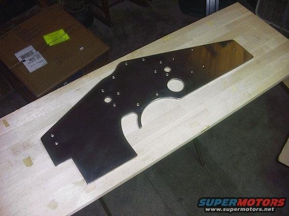 Polished metal engine part with multiple bolt holes on a wooden surface