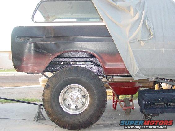 1978 Ford Bronco rear quarter panel with large tire, partially covered by a tarp