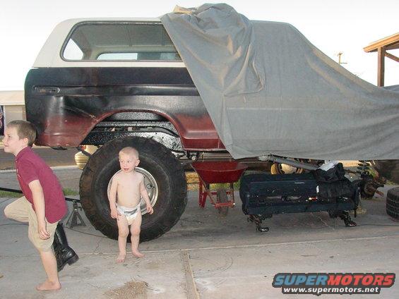 1978 Ford Bronco with large tires, partially covered, with two children nearby