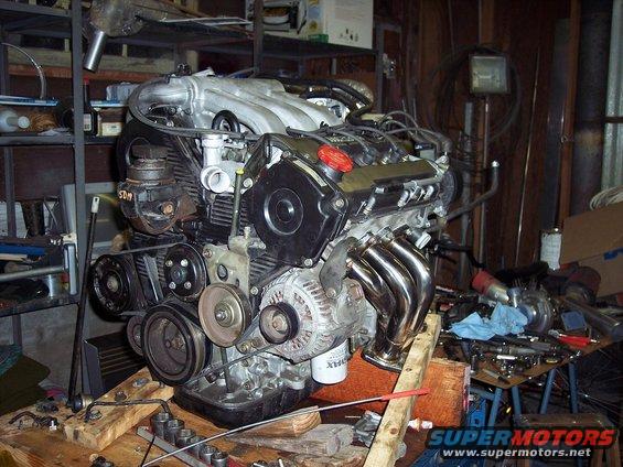 Engine with chrome exhaust headers, on a wooden stand in a workshop