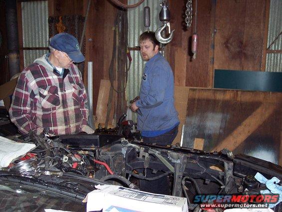 Two guys looking at an open car engine bay in a garage