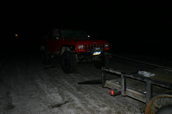 red Jeep Cherokee XJ with lifted suspension and large tires, hooked to a trailer at night
