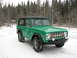 1975 Ford Bronco - A green 1975 Ford Bronco sits in a snowy landscape, its front grille and lights clearly visible.