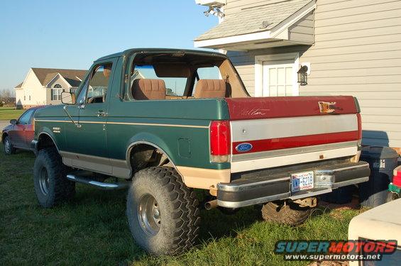 Green and tan 1987 Ford Bronco with red tailgate, lifted suspension, and large tires