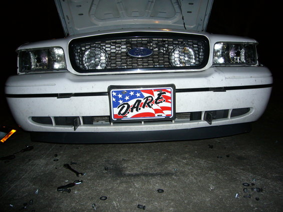 Front view of a white Ford Crown Victoria with its hood up. It has a D.A.R.E. license plate
