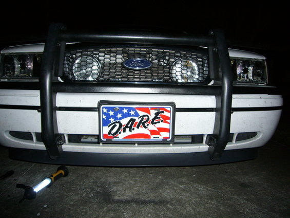 White Ford Crown Victoria front end with a black push bar, honeycomb grille, and a D.A.R.E. license plate