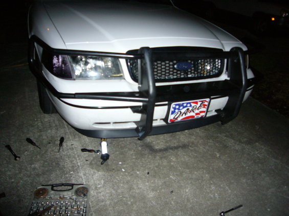 2000 Ford Crown Victoria front end with push bar and DARE license plate. Tools on the ground