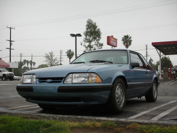 Blue 1990 Ford Mustang coupe, 3q-front view. Text 'MUSTANG' visible on front