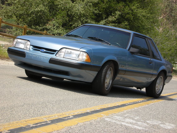Blue 1990 Ford Mustang coupe parked on a road with yellow lines