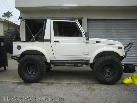 White 1987 Suzuki Samurai side view with off-road tires and a roll cage
