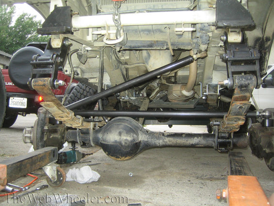 Close-up of leaf springs, differential, and steering linkage on a vehicle undergoing modification