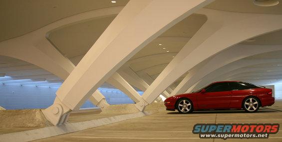 Red 1993 Ford Probe parked under a white, curved architectural structure