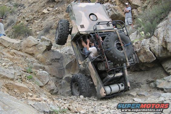 Off-road vehicle on its side on a steep, rocky slope with two people watching