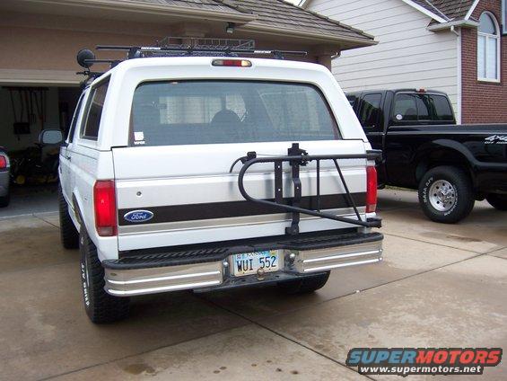 Rear view of a white Ford Bronco with a spare tire carrier and a black Ford pickup truck parked nearby