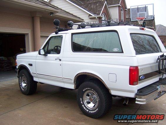 White Ford Bronco SUV with roof rack and aftermarket lights, parked in driveway