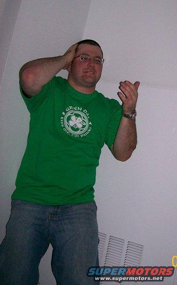 Man in green t-shirt with shamrock logo and jeans, hands on head