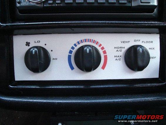 Interior climate controls with three knobs and labels for fan speed, temperature, and air direction