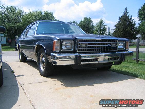 Dark blue sedan parked on concrete driveway, front 3/4 view. Chrome grille and bumper are prominent