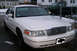 1999 Ford Crown Victoria - Front view of a white sedan with a chrome grille, parked in a residential area.