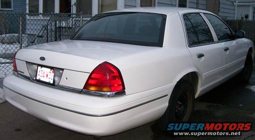 White 1998 Ford Crown Victoria, rear 3/4 view, showing damage on the rear bumper and a dent on the driver's side rear door