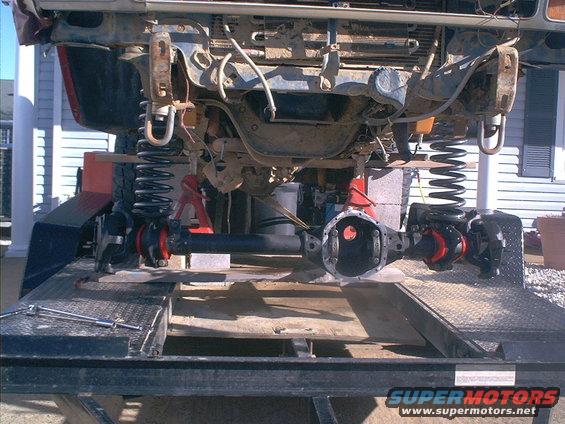 Front axle assembly with differential removed, suspension springs, and frame components, resting on a trailer