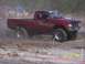 1989 Ford Bronco - A lifted red pickup truck navigates a dusty off-road course with onlookers present.