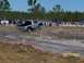 1989 Ford Bronco - A silver pickup truck navigates a dirt track during an event, with spectators watching from the sidelines.