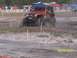 1989 Ford Bronco - Jeep Wrangler navigates a muddy off-road course with a crowd watching.