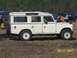 1989 Ford Bronco - A cream-colored Land Rover Series III station wagon is parked outdoors with other vehicles in the background.