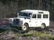 1989 Ford Bronco - A white Land Rover Defender navigates a rough terrain course on a sunny day.