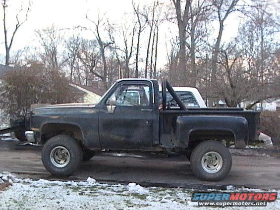 Black pickup truck with a roll bar and a white vehicle behind it, seen from the side