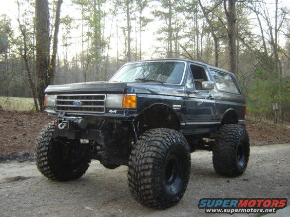 Black Ford Bronco with large off-road tires and winch, parked on a dirt road