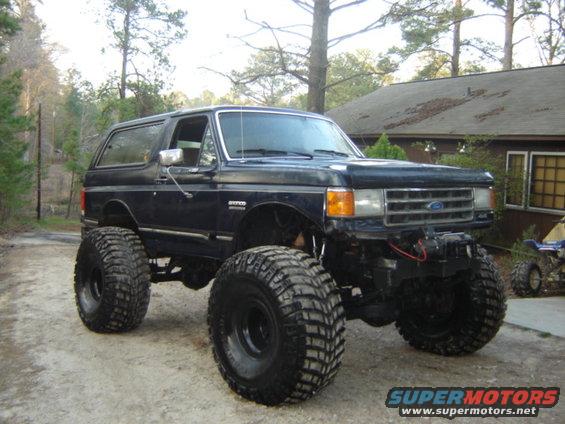 1989 Ford Bronco modified with a lift kit and oversized off-road tires parked on a dirt driveway