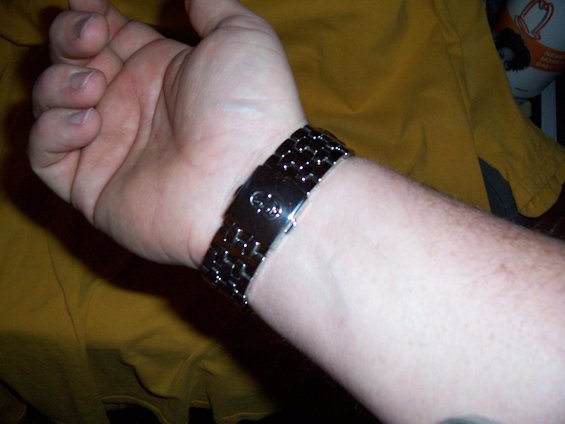 Wrist wearing a metal band watch with a circular emblem on the clasp