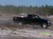1989 Ford Bronco - A black Nissan pickup truck drifts on a dirt track, creating a cloud of dust. Other vehicles and trees are visible in the background.