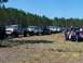 1989 Ford Bronco - Several lifted trucks and SUVs are parked in a grassy field with trees in the background.