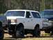 1989 Ford Bronco - A white 1989 Ford Bronco is shown with a lifted suspension and large off-road tires, parked outdoors.