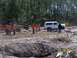 1989 Ford Bronco - A white SUV is positioned on a dirt obstacle course, with a backhoe and several people in the background.