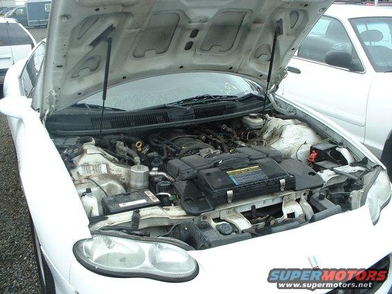White car's engine bay with hood open. Visible engine components and battery