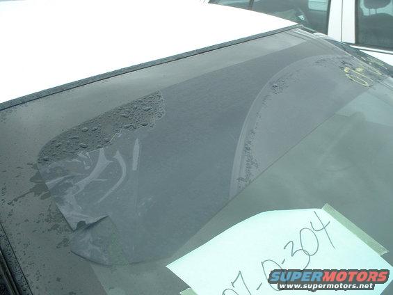 Windshield with peeling tint and water spots, paper with writing taped to it, Supermotors logo visible