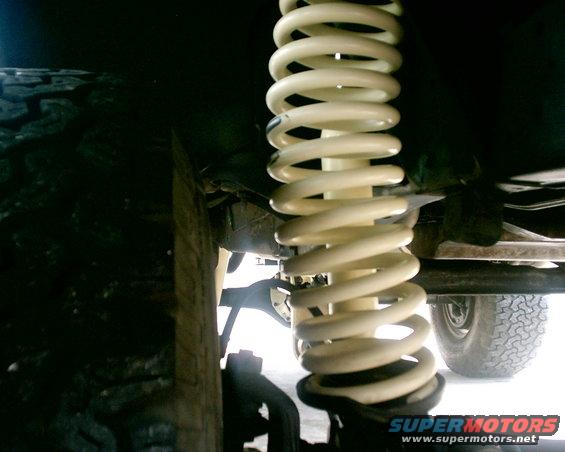Close-up of a white coil spring and part of a tire on a vehicle