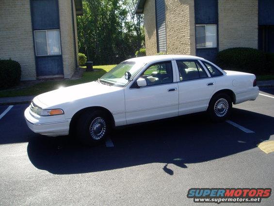 White sedan parked in a lot, 3/4 front view. Appears to be a 1998 Ford Crown Victoria