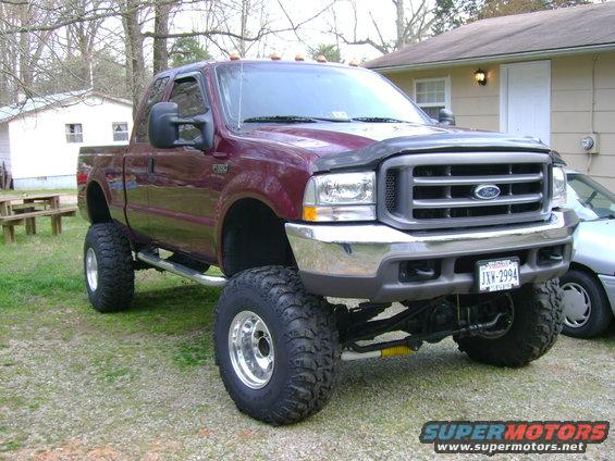 Maroon Ford F-350 pickup truck with large tires and lift kit parked in a yard