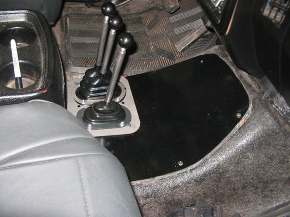 Interior view of a vehicle's center console showing three gear shifters and a cup holder with a marker